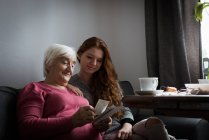 Grandmother and granddaughter looking at photograph in living room at home — Stock Photo