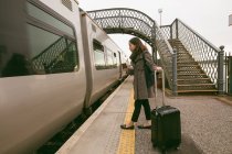 Woman getting in the train with luggage at railway platform — Stock Photo
