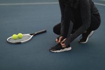 Молодая женщина завязывает шнурки на теннисном корте — стоковое фото
