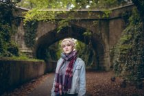 Thoughtful young woman  in warm clothing standing on path at park — Stock Photo