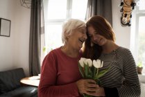 Lächelnde Oma und Enkelin stehen mit Blumen im heimischen Wohnzimmer — Stockfoto