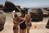 Rear view of siblings taking selfie with mobile phone on beach — Stock Photo