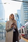 Donna in hijab utilizzando il cellulare alla stazione ferroviaria — Foto stock