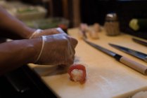 Chef rolando filetes de peixe sobre bola de sushi em uma tábua de corte — Fotografia de Stock