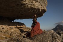 Масаи в традиционной одежде сидит на скале — стоковое фото