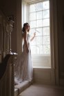 Jolie mariée debout à la fenêtre à la maison — Photo de stock