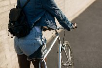 Vista trasera de la mujer caminando con su bicicleta en una acera - foto de stock