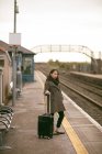 Mulher esperando o trem com bagagem na plataforma ferroviária — Fotografia de Stock