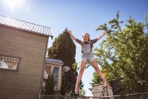 Girl jumping on trampoline in garden in countryside. — Stock Photo