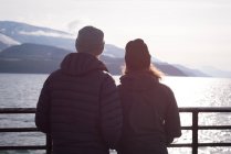 Пара смотрит на реку, стоящую у реки зимой — стоковое фото