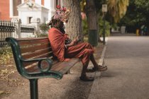 Maasai man in traditional clothing using mobile phone while relaxing on bench — Stock Photo