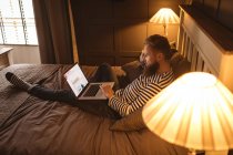 Чоловік лежить на ліжку, використовуючи ноутбук вдома — стокове фото