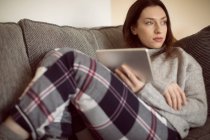 Donna che riposa con tablet digitale sul divano in soggiorno a casa . — Foto stock