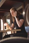 Чоловік розмовляє на мобільному телефоні, маючи каву у відкритому кафе — стокове фото