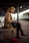 Giovane donna che elenca la musica mentre utilizza il suo telefono cellulare alla piattaforma ferroviaria — Foto stock