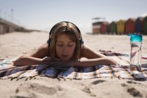 Дівчина-підліток слухає музику на навушниках, розслабляючись на пляжі в сонячний день — стокове фото