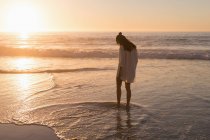 Mulher de pé na água do mar na praia ao entardecer . — Fotografia de Stock
