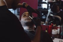 Мужчина сбривает бороду бритвой в парикмахерской — стоковое фото