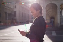 Woman using mobile phone while having drink on street — Stock Photo
