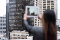 Visão traseira de empresária fotografando arranha-céus com seu tablet — Fotografia de Stock