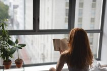 Visão traseira da mulher lendo um livro em casa — Fotografia de Stock