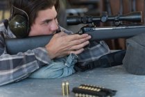 Seitenansicht eines Mannes, der mit dem Scharfschützengewehr auf Zielscheibe im Schießstand zielt — Stockfoto