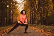 Mujer sonriente realizando ejercicio de estiramiento en el bosque - foto de stock