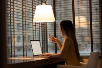 Бізнес-леді має каву під час роботи на ноутбуці в офісі — стокове фото