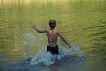 Rear view of boy playing in river on a sunny day — Stock Photo
