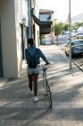Visão traseira da mulher andando com sua bicicleta em uma calçada — Fotografia de Stock