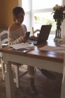Frau benutzt Handy bei der Arbeit am Laptop zu Hause — Stockfoto