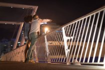 Romantic couple pointing at distance while standing near railing  at night — Stock Photo