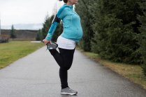 Mujer embarazada realizando ejercicio de estiramiento en el parque - foto de stock