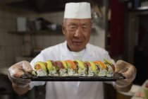 Senior chef holding tray of sushi in kitchen at hotel — Stock Photo