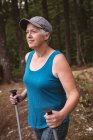 Femme mûre avec des bâtons de randonnée debout dans la forêt — Photo de stock
