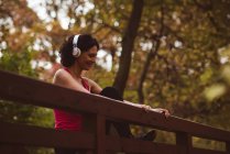Smiling woman enjoying music while exercising in forest — Stock Photo