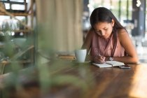Teenager schreibt im Restaurant an einem Tagebuch — Stockfoto