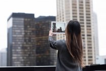 Rückansicht einer Geschäftsfrau, die Wolkenkratzer mit ihrem Tablet fotografiert — Stockfoto