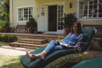 Frau liest Buch auf Sessel im Garten — Stockfoto
