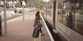 Femme monter dans le train avec des bagages au quai ferroviaire — Photo de stock