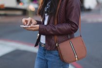 Средняя часть женщины, использующая мобильный телефон на городской улице — стоковое фото