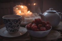 Close-up of teapot, cup and bowl of strawberries against lit candles — Stock Photo