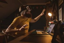 Человек в наушниках виртуальной реальности сидит перед ноутбуком дома — стоковое фото
