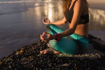 Cropped view of fit woman meditating on shore at dusk. — Stock Photo