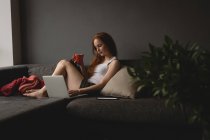 Mulher usando laptop enquanto toma café em casa — Fotografia de Stock
