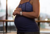 Partie médiane de la femme enceinte utilisant smartwatch à la maison — Photo de stock