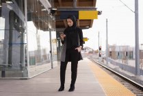 Femme en hijab utilisant un téléphone portable à la gare — Photo de stock