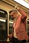 Чоловік стоїть за допомогою мобільного телефону під час подорожі в поїзді — стокове фото