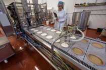 Lavoratrice che controlla il cibo vicino alla linea di produzione nella fabbrica alimentare — Foto stock