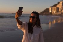 Mulher tomando selfie com telefone celular na praia ao entardecer . — Fotografia de Stock